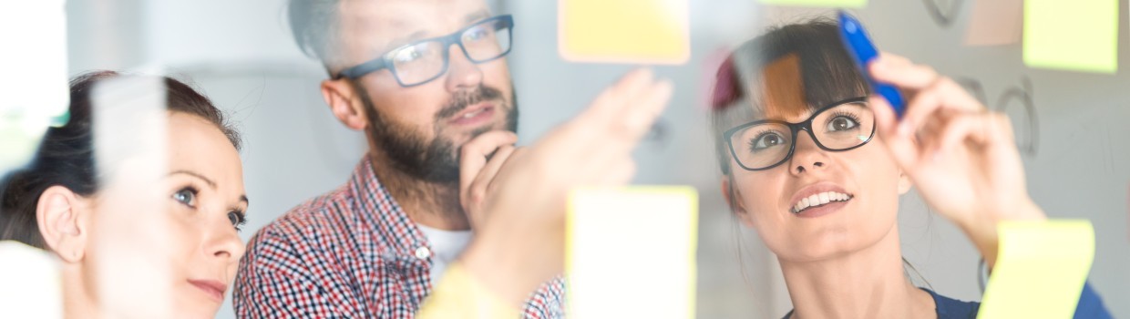 3 Personen schauen auf eine Wand mit Post-its