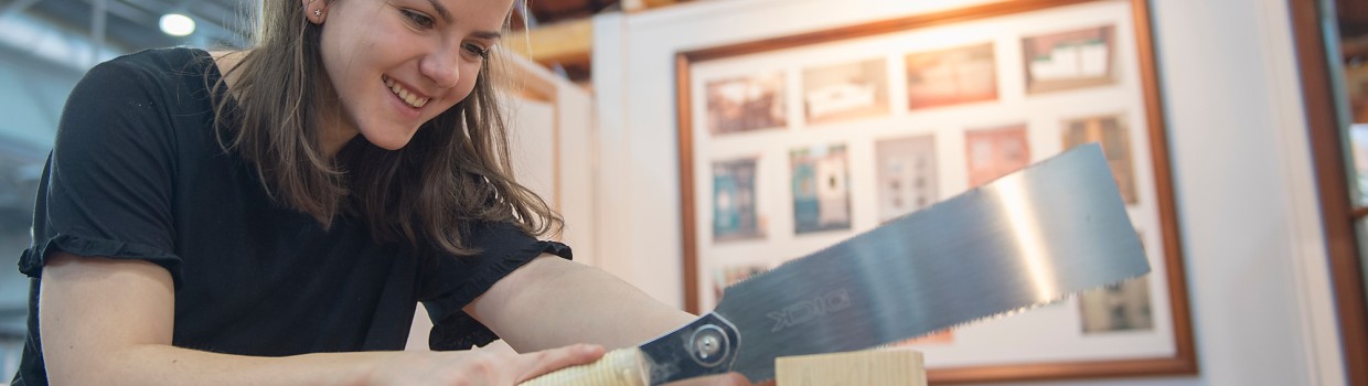 Eine Frau bearbeitet mit einer Säge ein Stück Holz