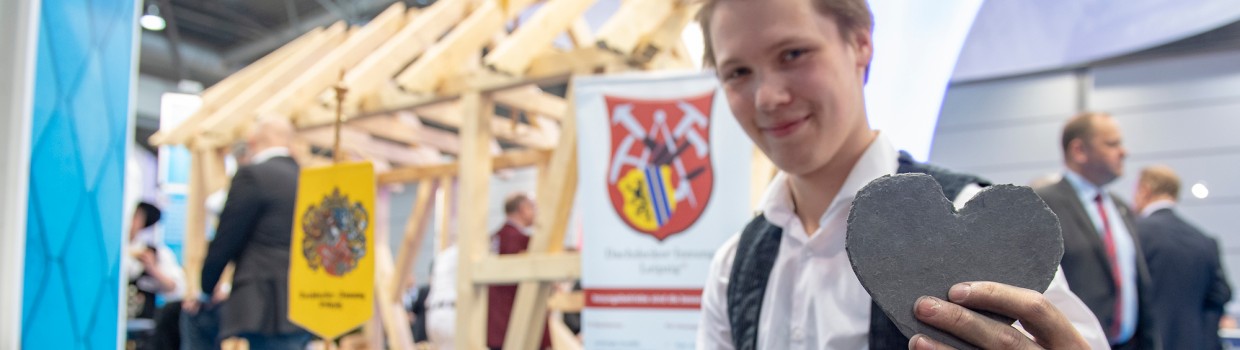 Ein Handwerk zeigt an aus Schiefer gearbeitetes Herz in die Kamera.