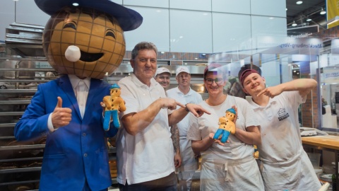 Das Leipziger Messemännchen steht zusammen mit einer Gruppe von Bäckern zusammen. Sie zeigen ein Brotmännchen in die Kamera was dem Leipziger Messemänchen gleicht.