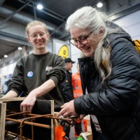 Eine Frau arbeitet zusammen mit einer Handwerkerin an Metall