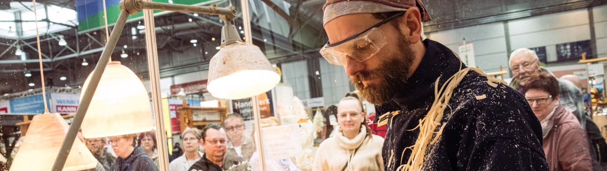 Ein Handwerker arbeit vor Besuchern an einer Holzmaschine.