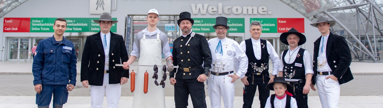 9 Personen aus dem Handwerk stehen vot der Glashalle der Leipziger Messe.