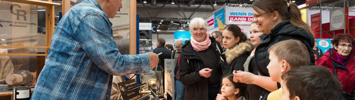 2 Frauen und eine Gruppe von Kindern stehen an einem Verkaufsstand für Werkzeuge. Ein Mann berät die Gruppe.